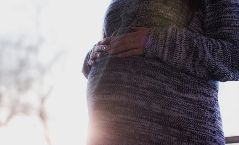 woman holding her prenant tummy during daytime