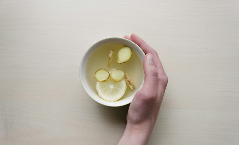 person holding white bowl with sliced lime and ginger inside